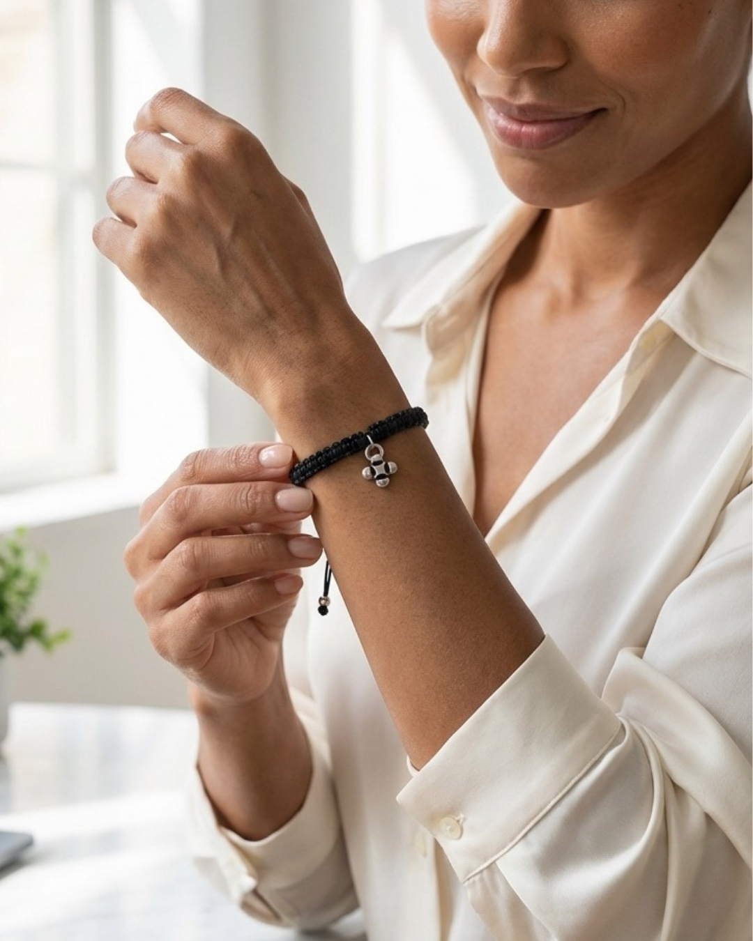 Woman adjusting a custom nonprofit charm bracelet with branded silver logo pendant on her wrist, worn over a black lace sleeve.