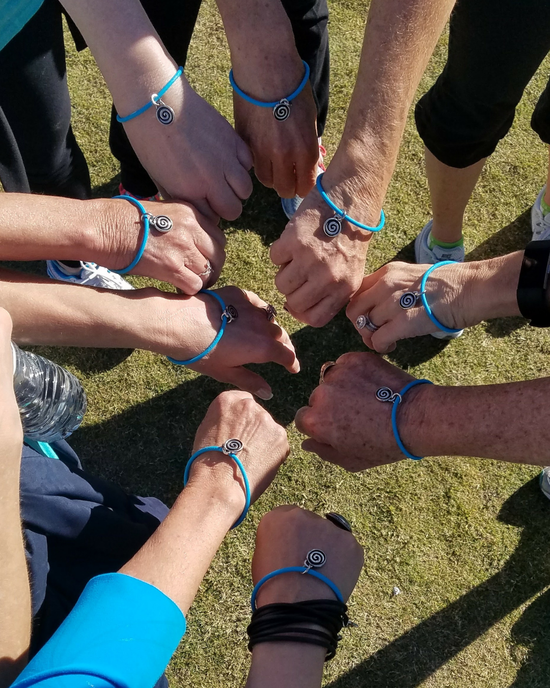 Group of nonprofit event participants showing matching custom charity bracelets with silver spiral charms on teal chords at an outdoor fundraising event.